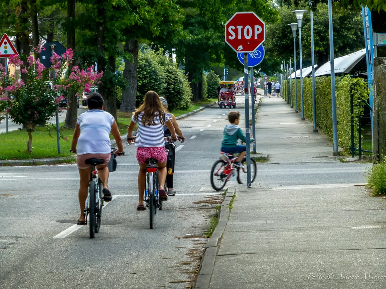 In this image we can see people riding bicycles and there are sign boards. In the background there...
