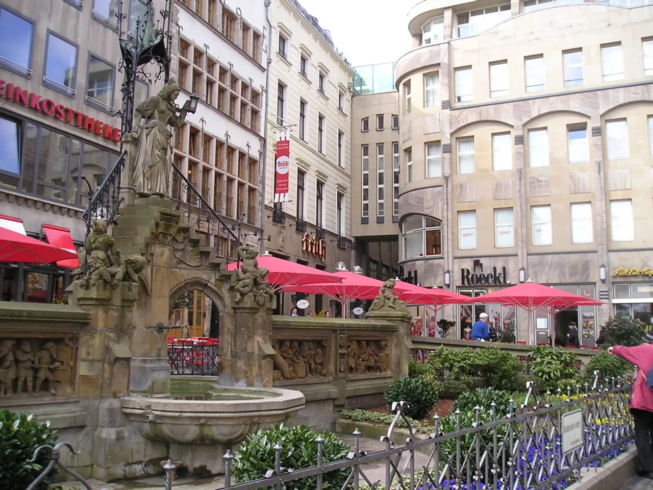 The picture is taken outside a city. In the foreground of the picture there are plants, railing,...