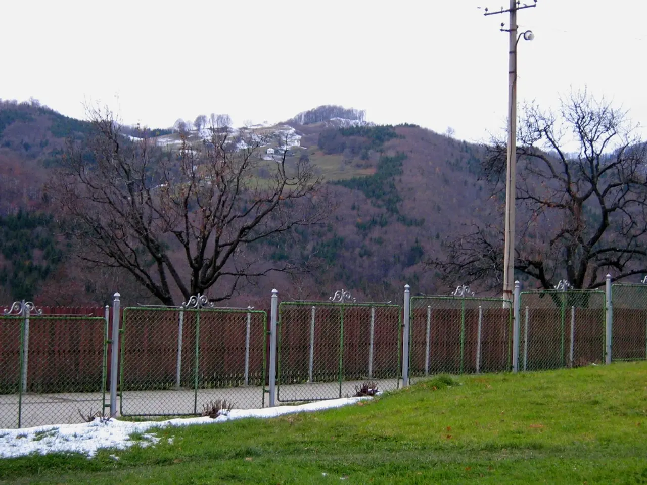 In this picture we can see grass, fence, pole and trees, and we can find few houses on top of the...