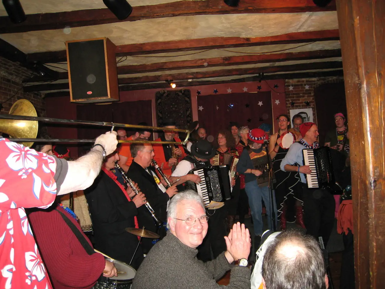 This picture shows the inner view of a building. There are some people sitting, three curtains...