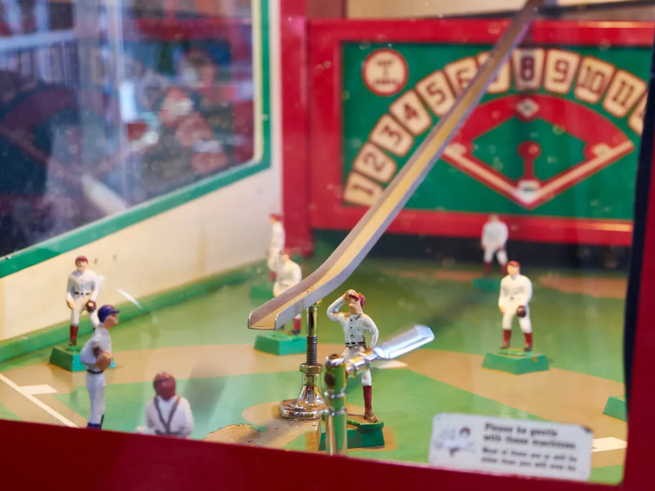 In this image there is a table baseball court with a few toys of men and there is a poster with a...