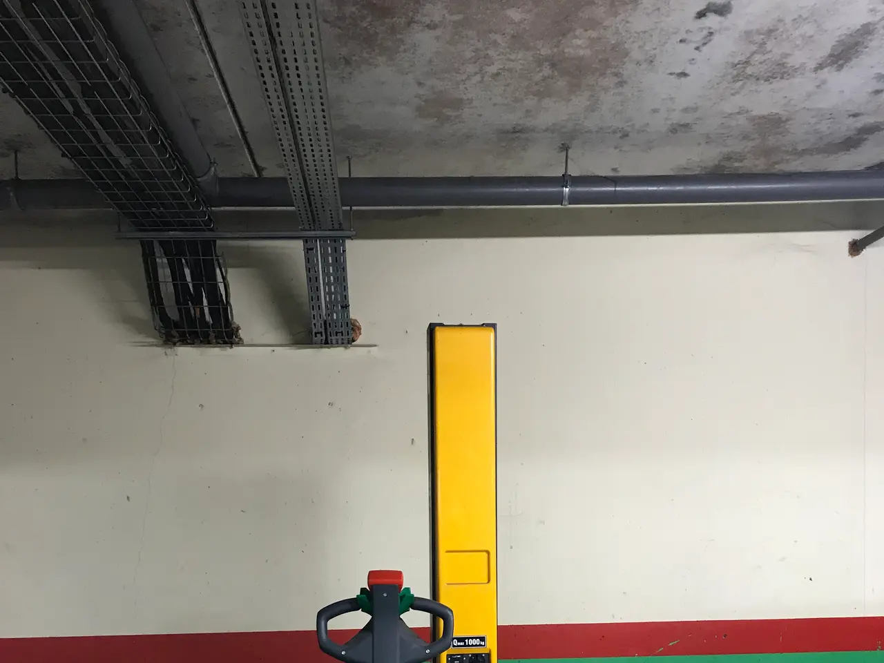 The image shows a yellow forklift parked in a warehouse, with metal racks on the left side and a...