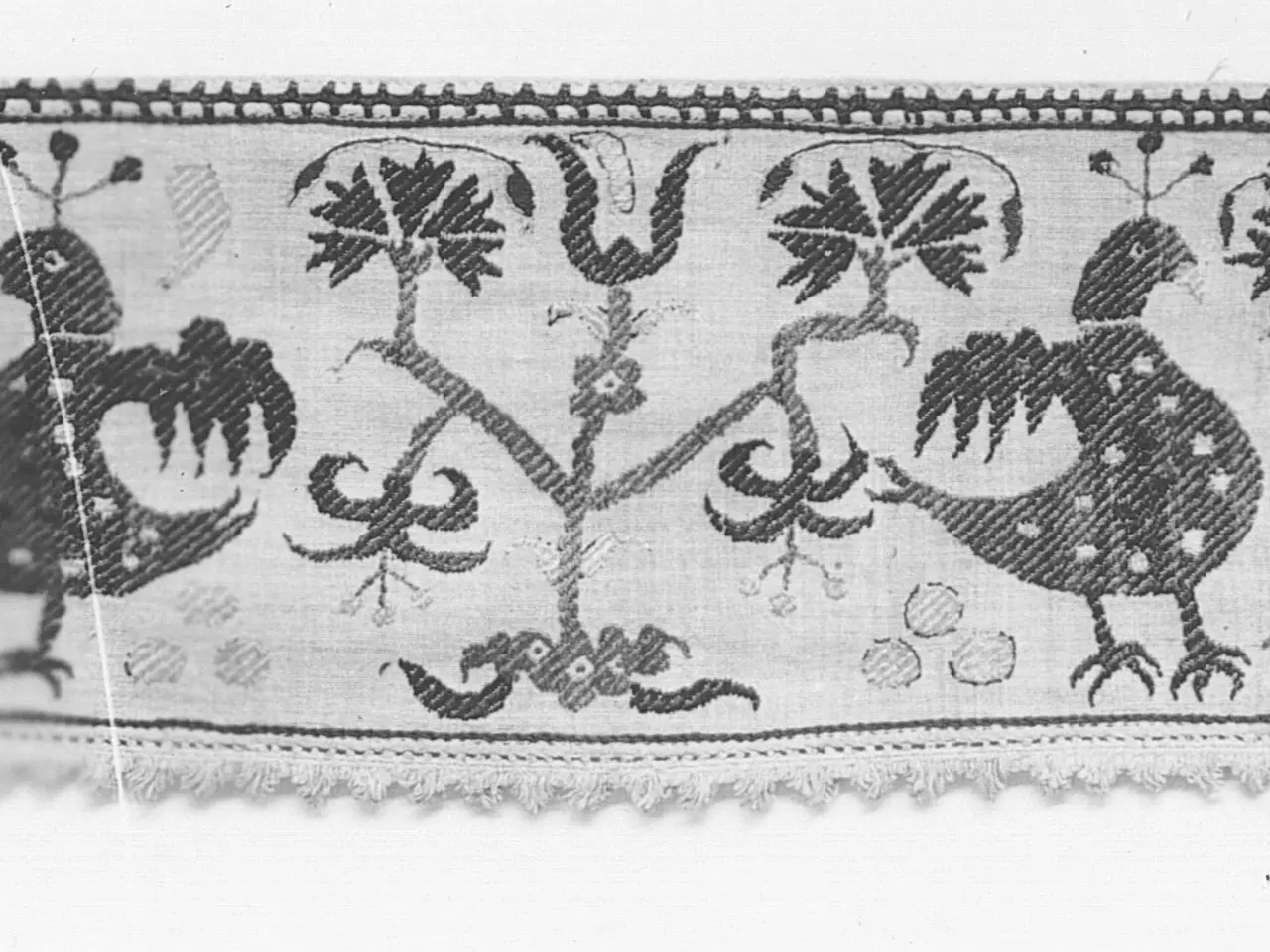 The image shows a black and white photo of a textile with a pattern of birds and flowers. The...
