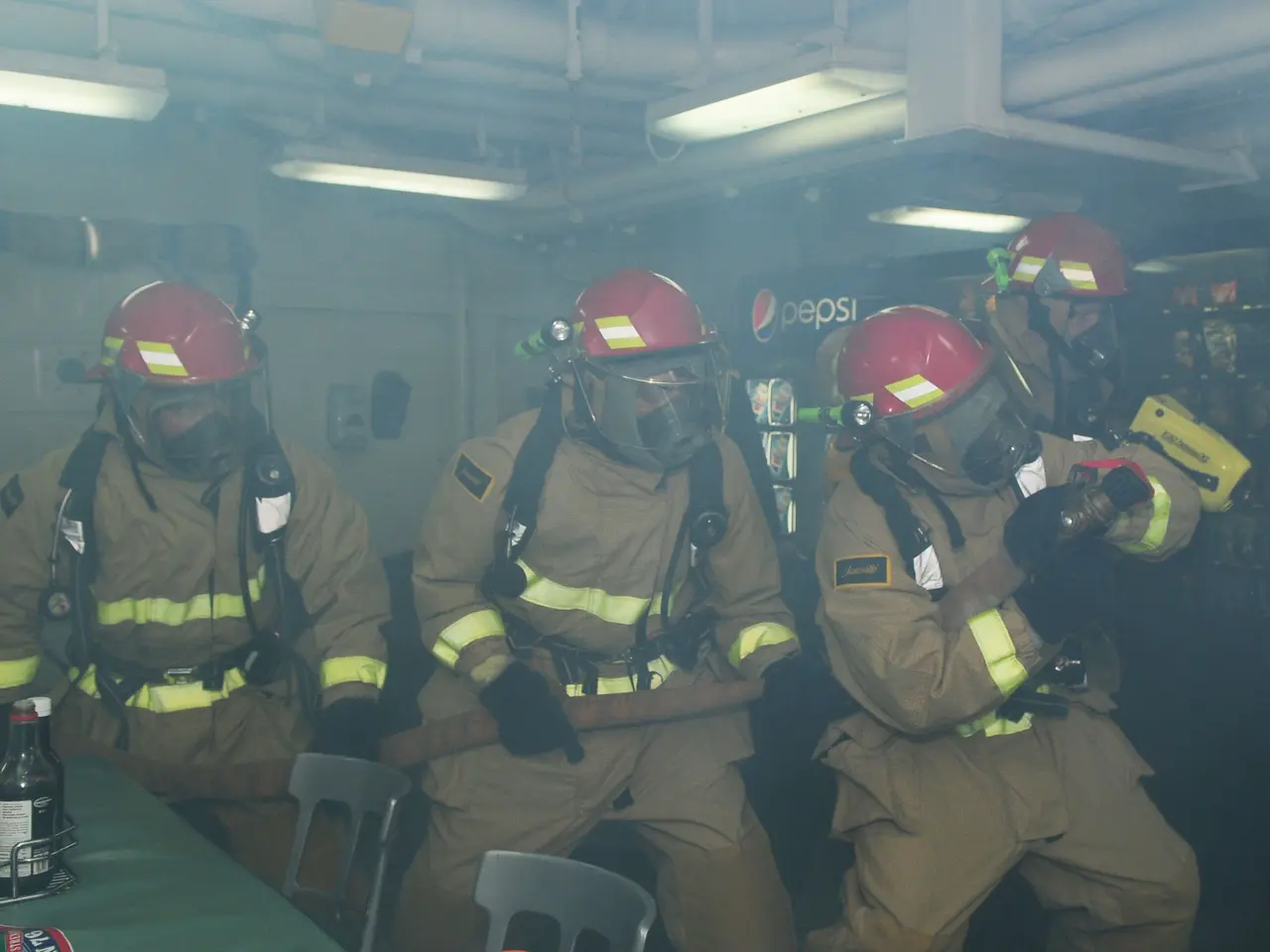 The image shows a group of firefighters wearing helmets and gas masks, sitting around a table with...