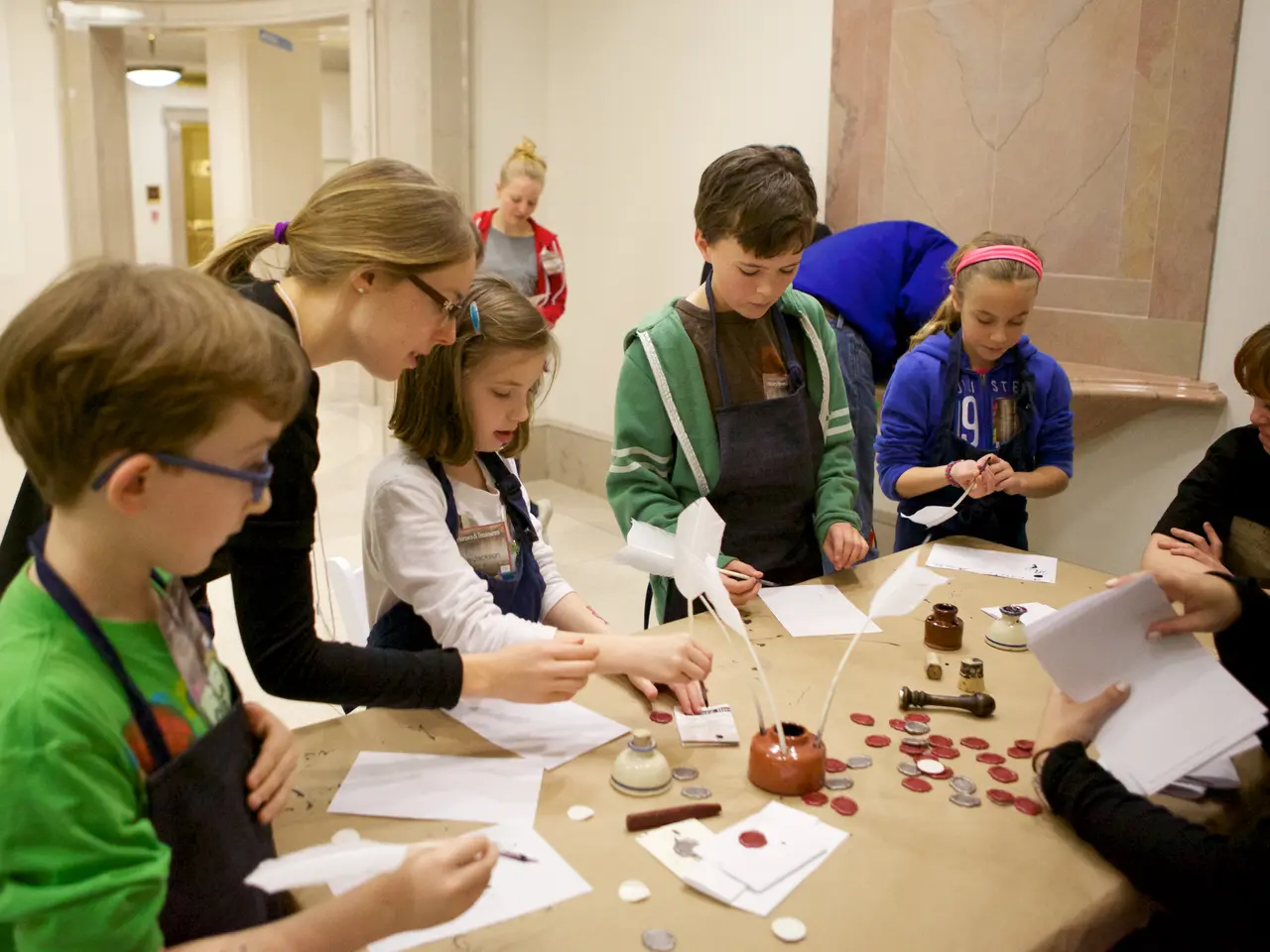 The image shows a group of children sitting around a table with papers, coins, and other objects...