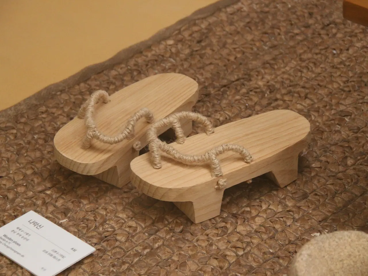 The image shows a pair of wooden slippers sitting on top of a rug, with a wooden object on the...