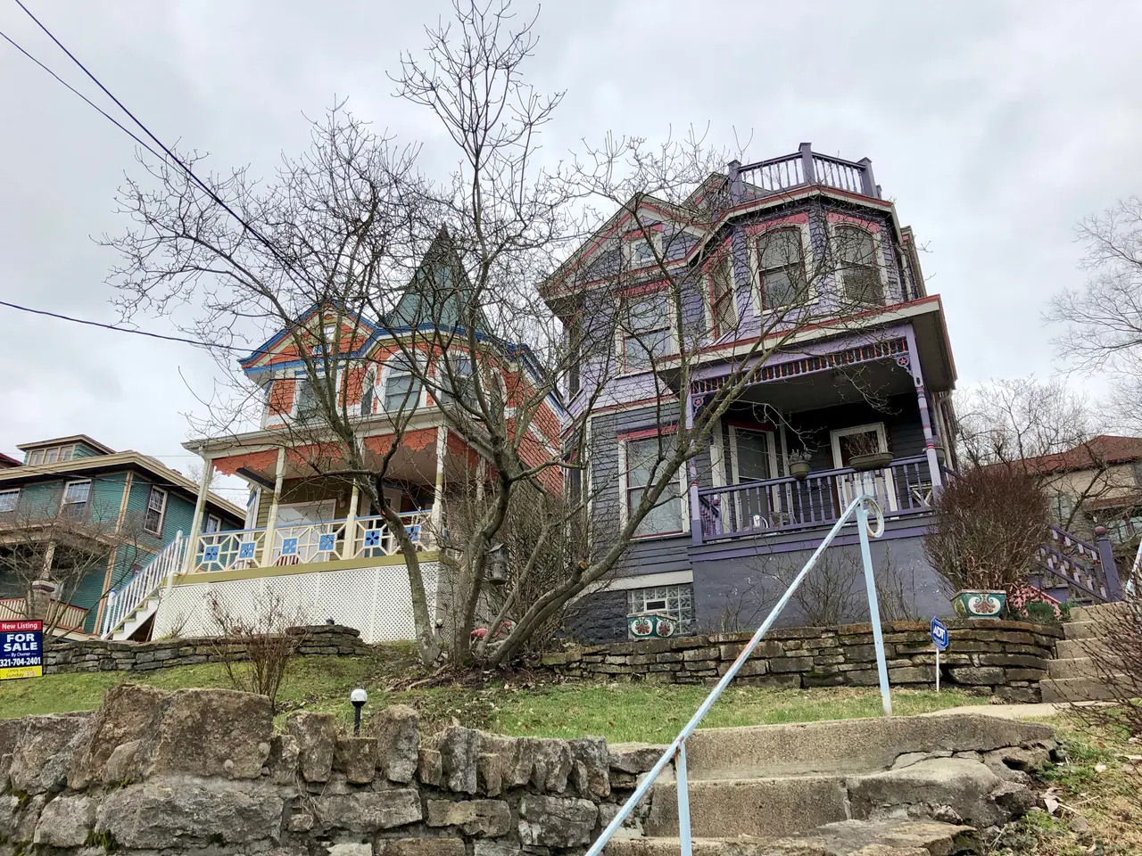 The image shows a row of Victorian-style houses on the corner of a street, with windows, railings,...