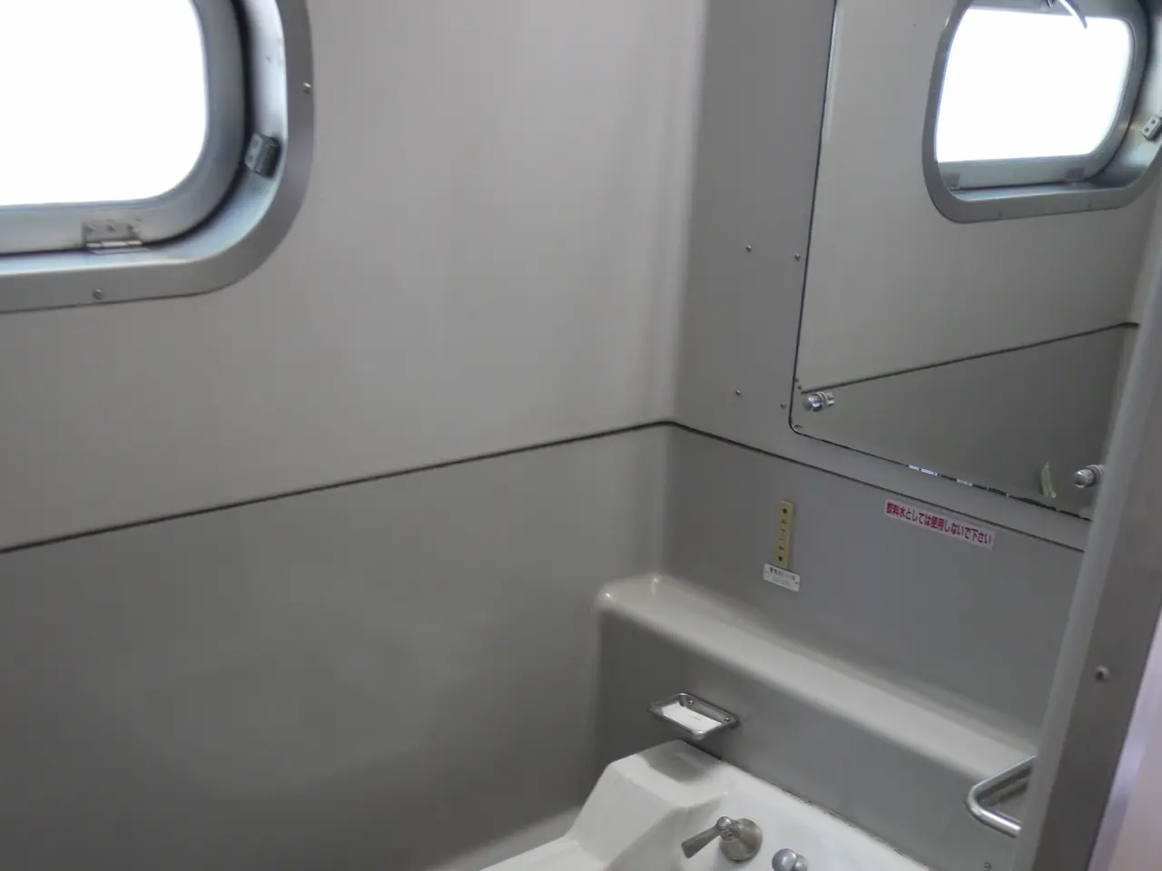 The image shows a small bathroom with a washbasin, taps, a mirror, a dustbin on the floor, and two...