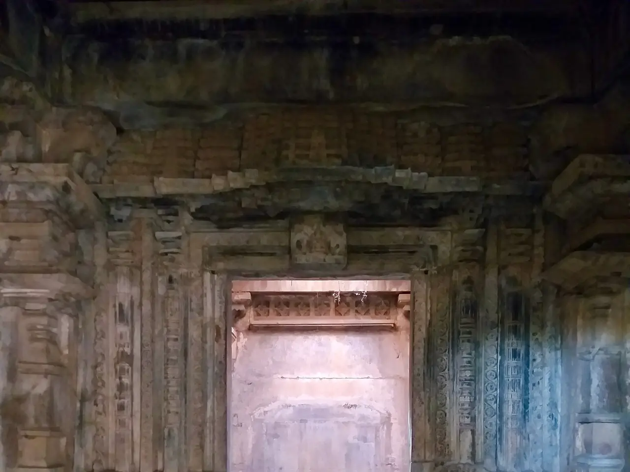 The image shows an old building with carvings on the walls and a doorway in the middle. The walls...