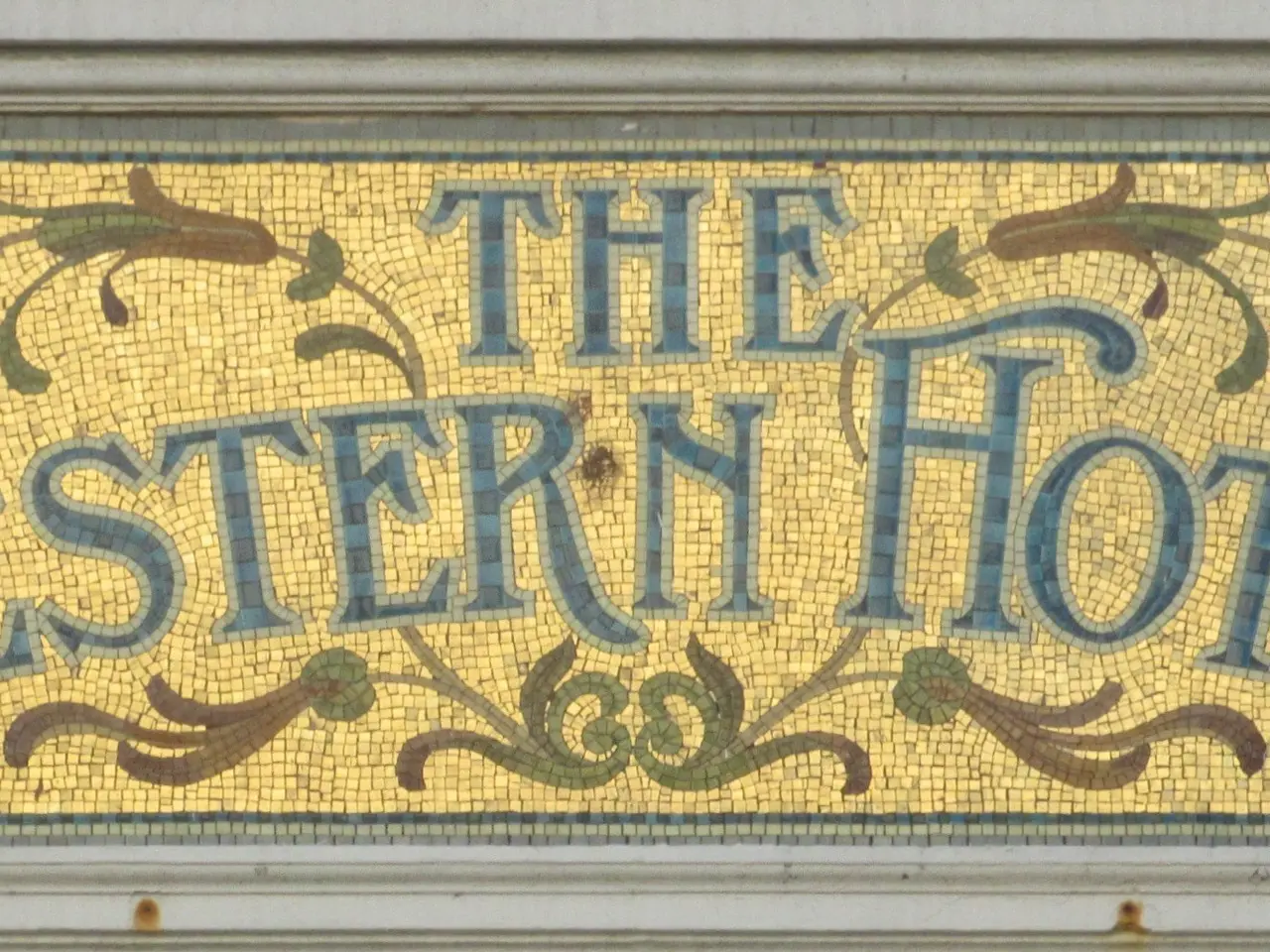 The image shows a wall with a mosaic sign that reads "The Western Hotel" in bold, black lettering....