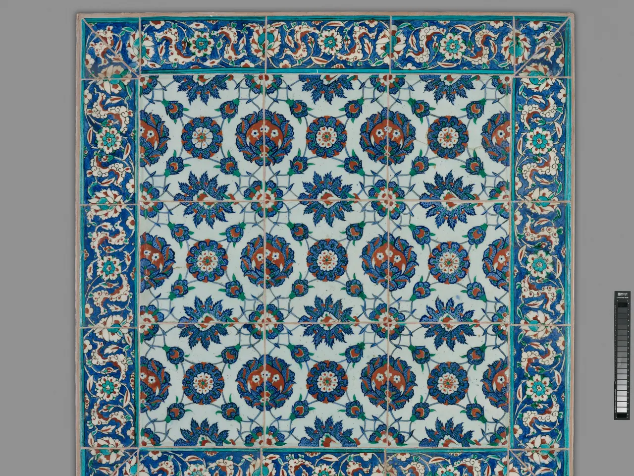 The image shows a blue and red tile with a floral design on it, set against a grey background. The...