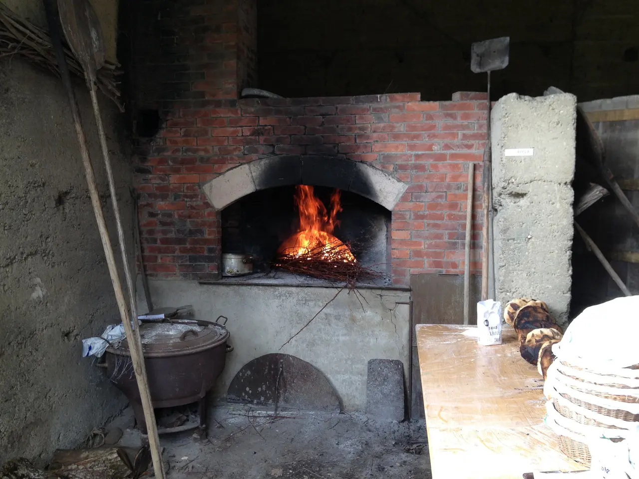 The image shows a brick oven with a fire burning inside of it. On the right side of the oven, there...