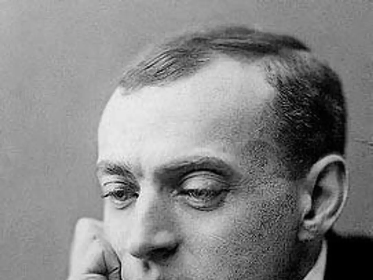 The image shows a black and white photo of a man in a tuxedo, with a wall in the background. The...