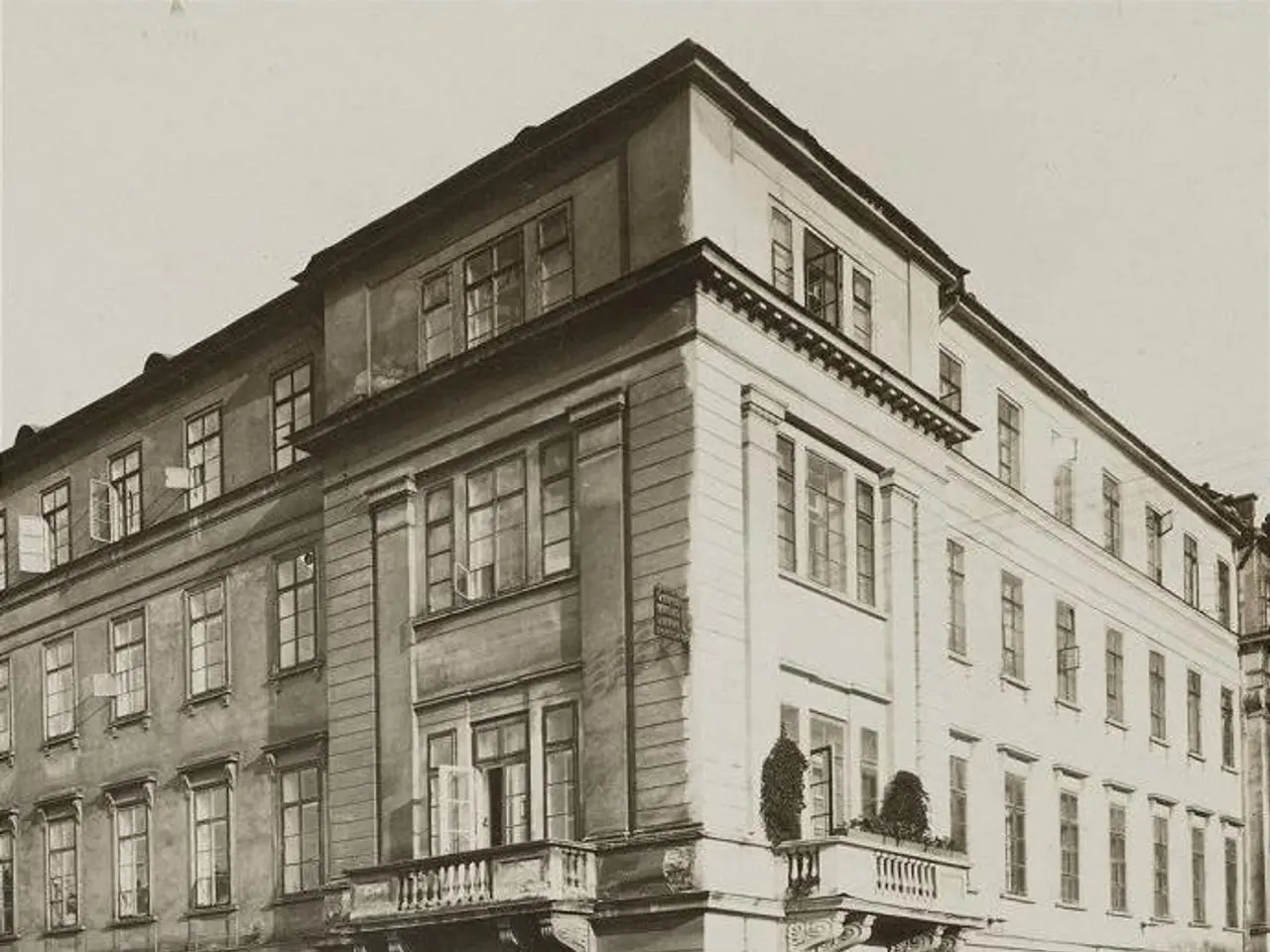 The image shows an old building with windows, steps with railings, boards with text, and pots with...