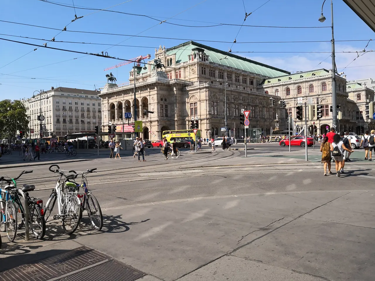 The image shows a bustling city street in Vienna, Austria, with many people walking and riding...