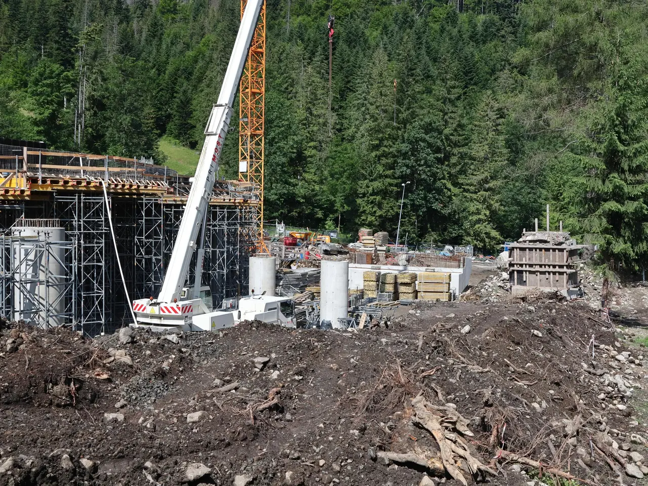 The image shows a construction site with a crane in the middle of it, surrounded by metal rods,...