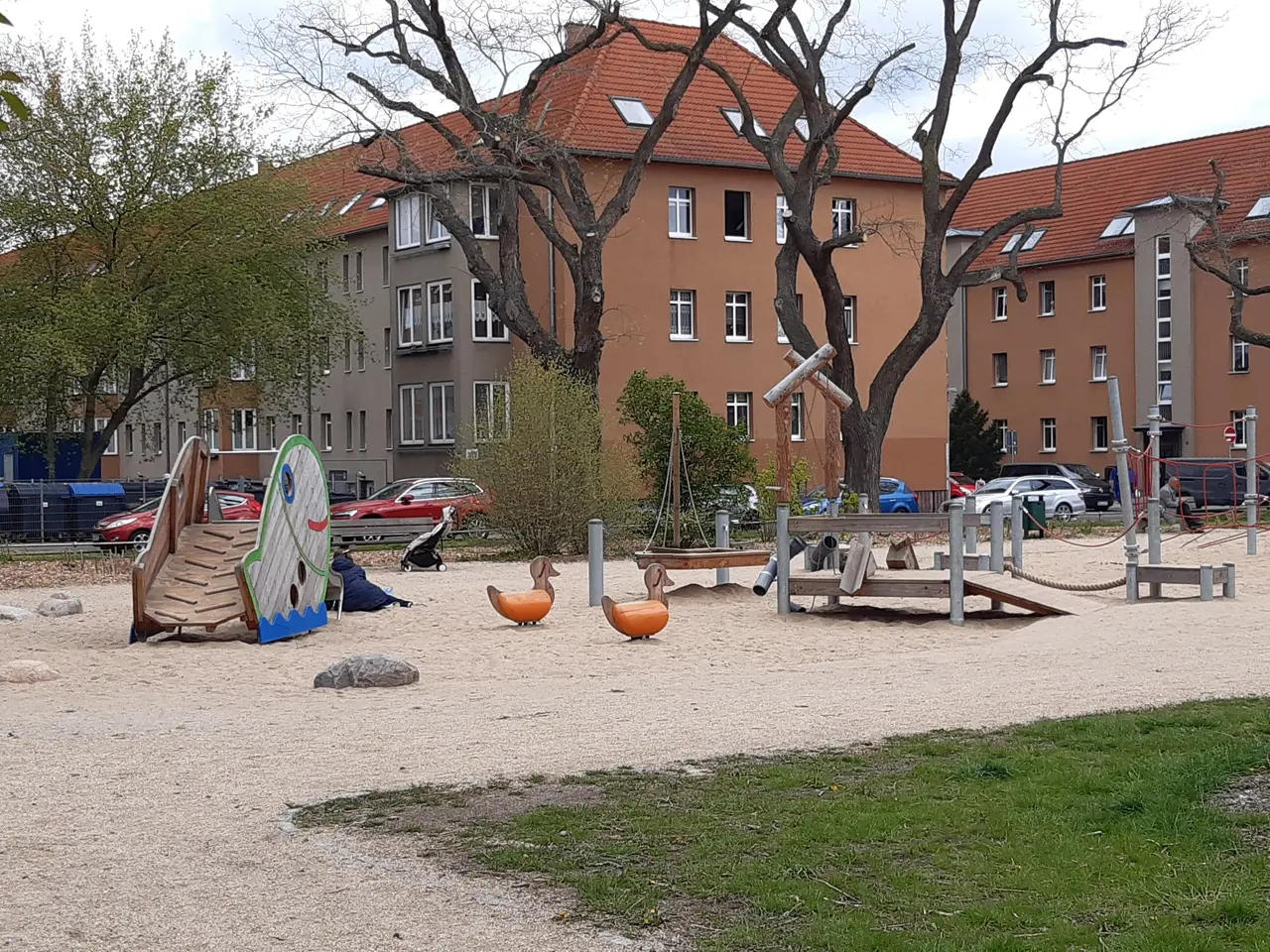 The image shows a playground in the middle of a park with a variety of toys, including a slide,...