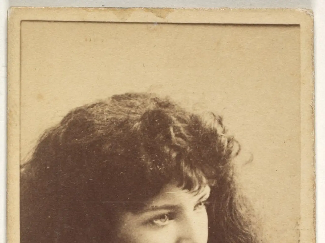 The image shows an old photo of a woman with long hair. She has a gentle expression on her face and...