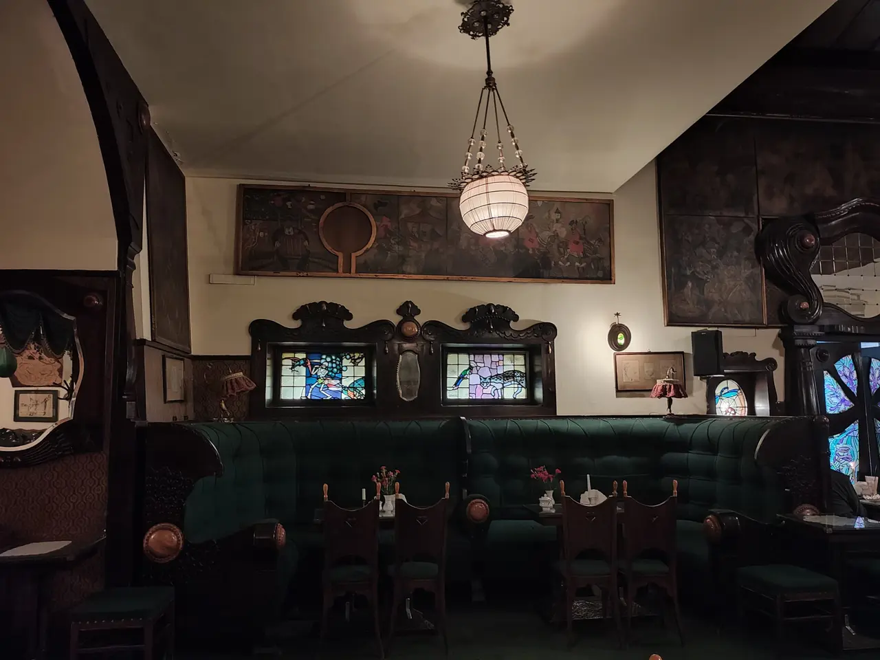 The image shows a room filled with lots of tables and chairs, flower vases on the tables, sofas, a...