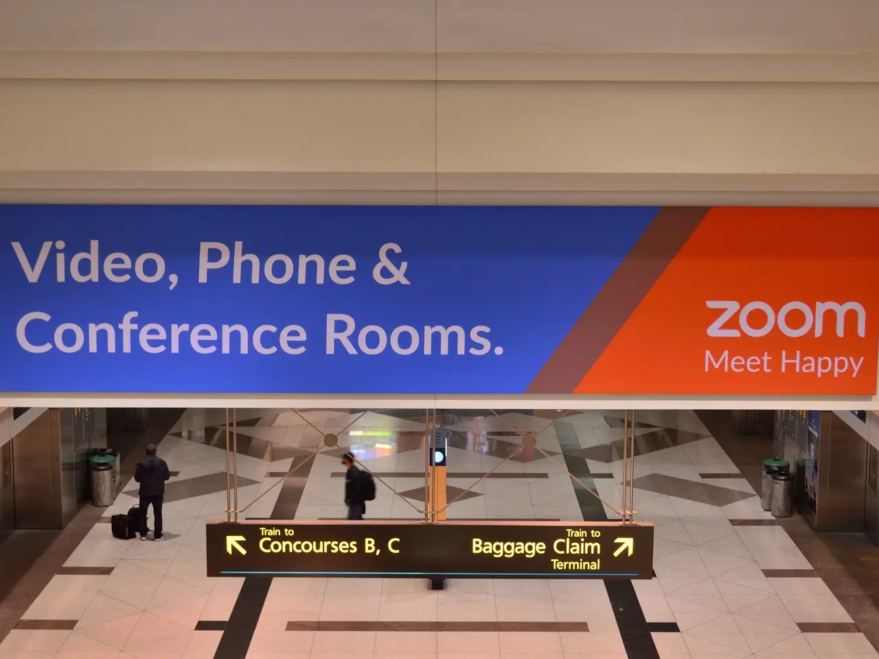 The image shows a bustling airport with people walking around, some of them carrying bags. There is...