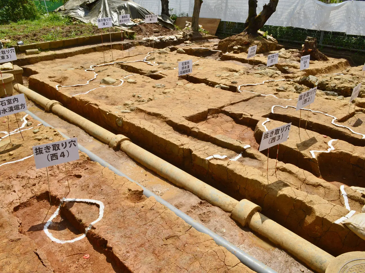 The image shows a large excavation site with a lot of dirt on the ground, surrounded by trees,...
