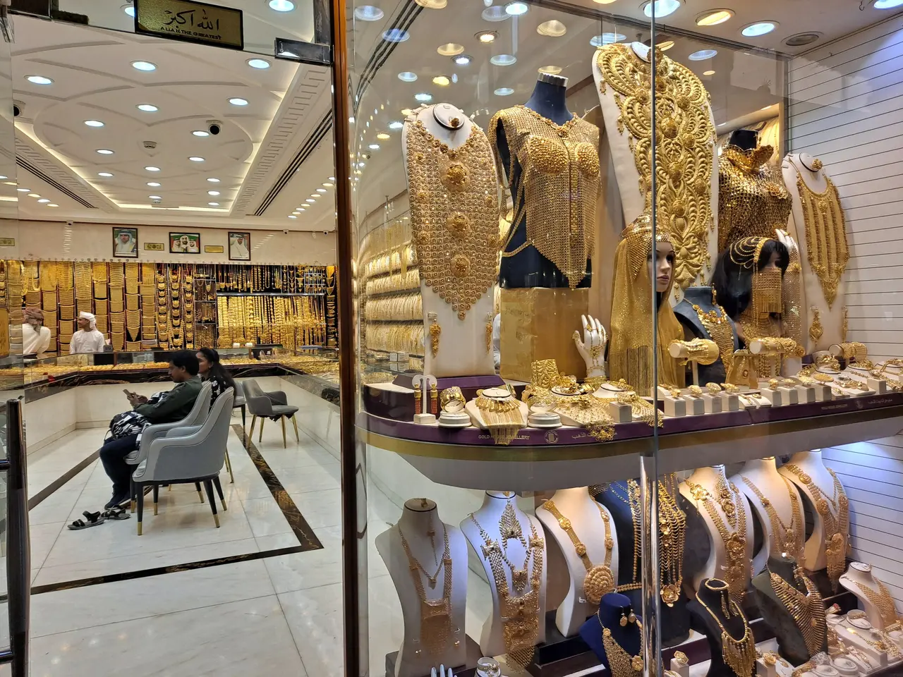 The image shows a store filled with lots of gold jewelry, including mannequins wearing ornaments,...