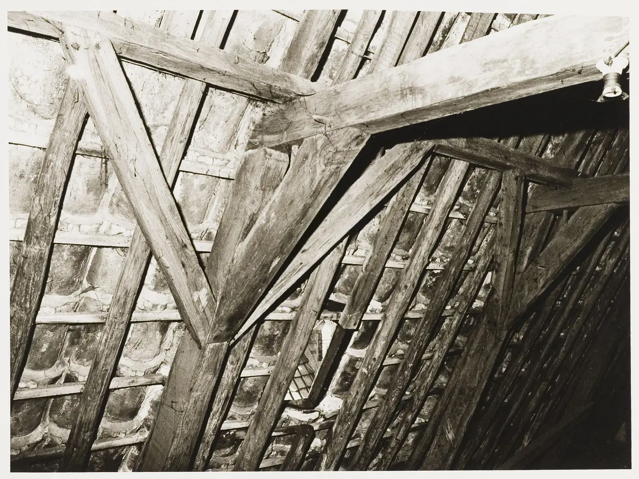 The image shows a black and white photo of an attic with wooden beams and a wall in the background....