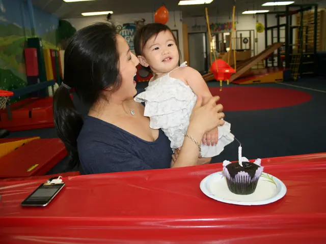 Here we can see a woman holding a baby. There is a table. On the table we can see muffins, plate,...
