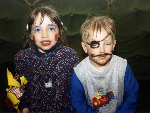 In this picture there are two persons standing and at the back there is a curtain.
