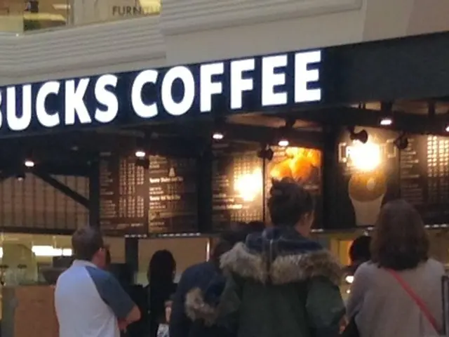 In front of the image there are people standing. In front of them there is a coffee shop. At the...