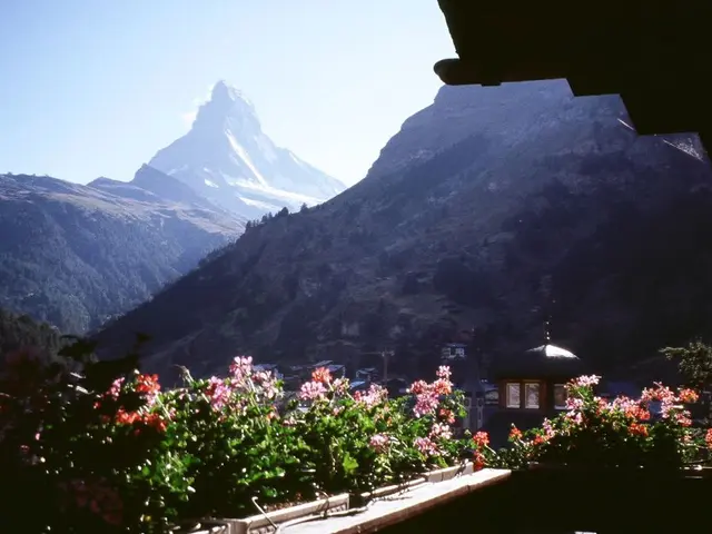 In this image we can see mountains, trees, buildings and sky.