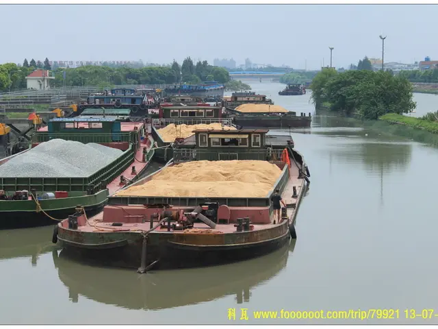 In the foreground of this image, there are boats with sand and stones on it on the water. On the...