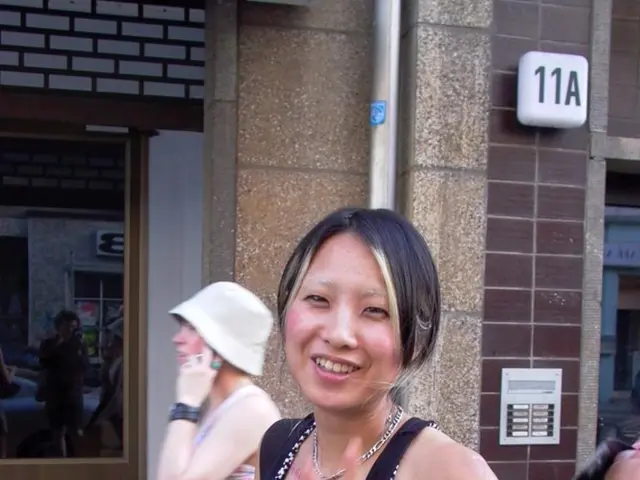 In this image we can see women standing on the road. In the background there are wall, pipeline and...