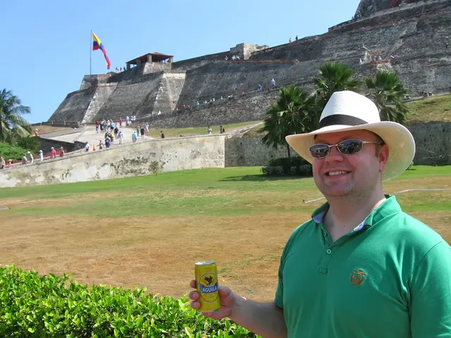 In the image there is a person standing on the left side in green t-shirt and holding a beer tin,...
