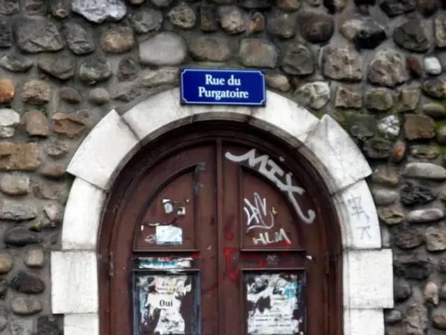 In this image we can see stone wall white color arch and brown color door on which there are some...