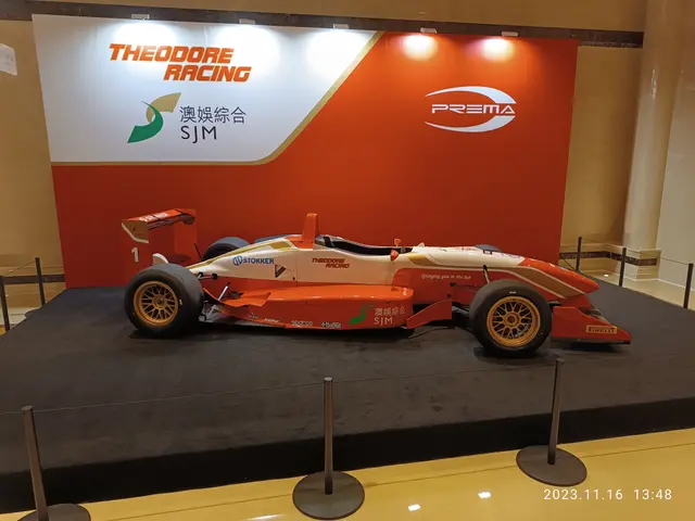 The image shows a red and white race car on display in a museum, surrounded by barrier poles with...