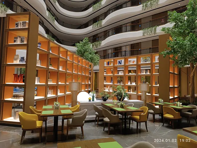 The image shows a large room filled with lots of tables and chairs, houseplants, lamps, books...