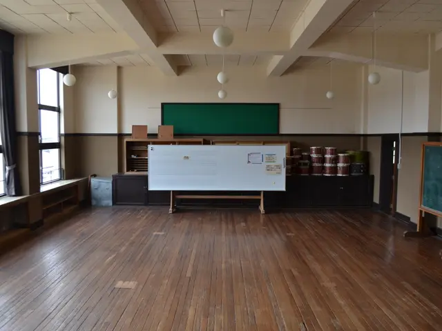 The image shows an empty classroom with wooden floors, a whiteboard on the wall, a table with...