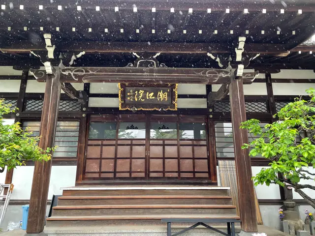 The image shows the entrance to a Japanese building with a wooden door and stairs leading up to it....