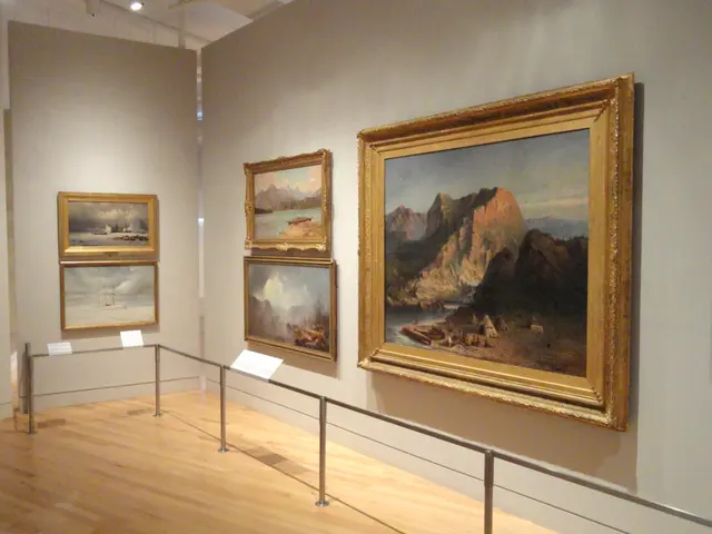 The image shows a room filled with lots of paintings on display, with photo frames on the walls, a...