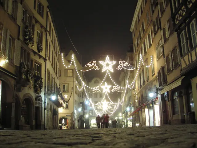 The image shows a cobblestone street in Strasbourg, France, illuminated by festive Christmas...