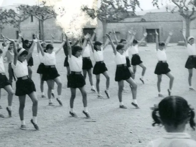 The image shows a group of young girls in school uniforms dancing in the street, surrounded by...