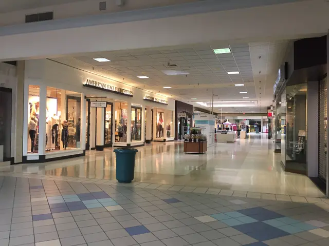 The image shows the inside of a shopping mall with a blue trash can in the middle. The floor is...