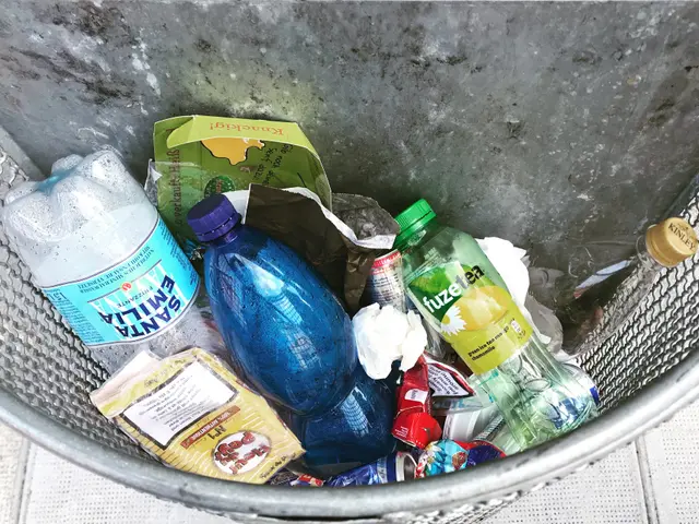 The image shows a metal trash can filled with a variety of plastic bottles, packets, and other...