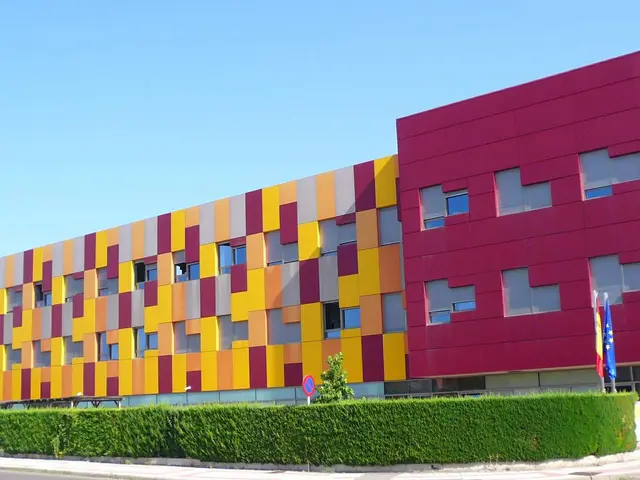 The image shows a colorful building with a lot of windows on the side of it, surrounded by street...