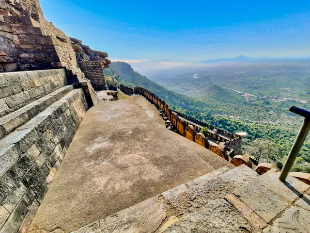 The image shows a set of stairs leading up to the top of a mountain, with a railing on the right...