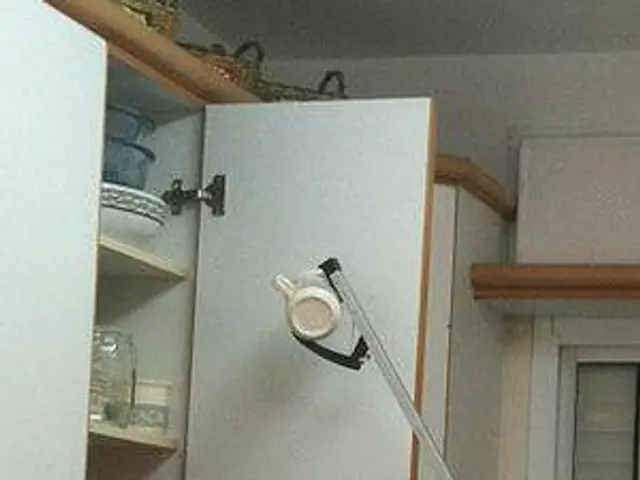 The image shows a person using a vacuum cleaner to clean a kitchen cabinet. The person is holding...