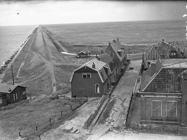 The image shows a black and white photo of a row of houses on the beach, with windows, poles,...