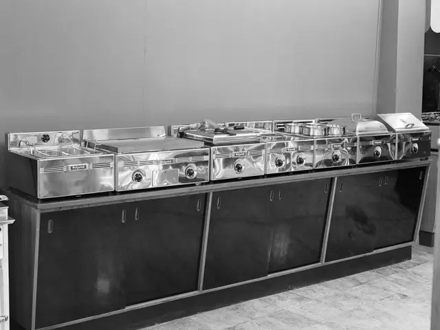 The image shows a black and white photo of a kitchen with a countertop featuring cupboards and a...