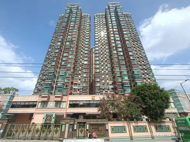 The image shows a tall building with many windows in the middle of a street, surrounded by trees,...